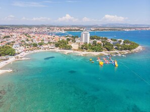 An aerial view of a coastal town with a marina, clear turquoise waters, and a prominent white building. - Apartment Rose Garden (Rovinj)
