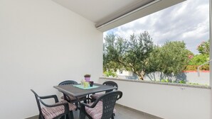 A balcony with a table and chairs, a potted plant, and a view of trees and a fence. - Apartment Rose Garden (Rovinj)