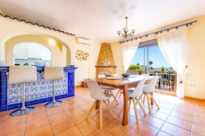 A dining area with a large table, white chairs, and a view of the outdoors. - Villa Ecalinda - Plusholidays (Calpe)