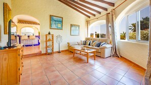 Amplia sala de estar con techo de madera, un sofá, una mesa de centro y vistas al exterior a través de grandes ventanales.