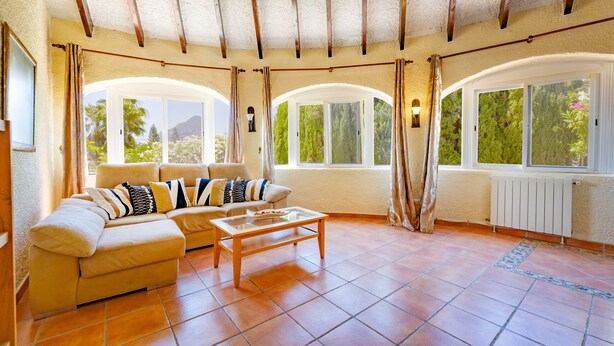 Amplia sala de estar con un sofá beige, una mesa de centro de madera y ventanas grandes con cortinas.