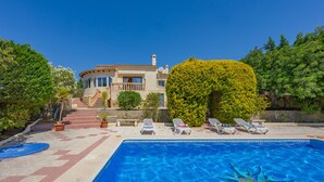 Una piscina con sillas de descanso, un camino de piedra y una casa con un gran árbol frente a ella.