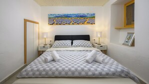 A neatly made bed with a patterned bedspread and two rolled towels, a painting above the bed, and a small window with a wooden frame. - House Miha (Tar-Vabriga)