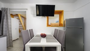 A compact kitchen with a white table, grey chairs, a black TV, and a grey refrigerator. - House Miha (Tar-Vabriga)