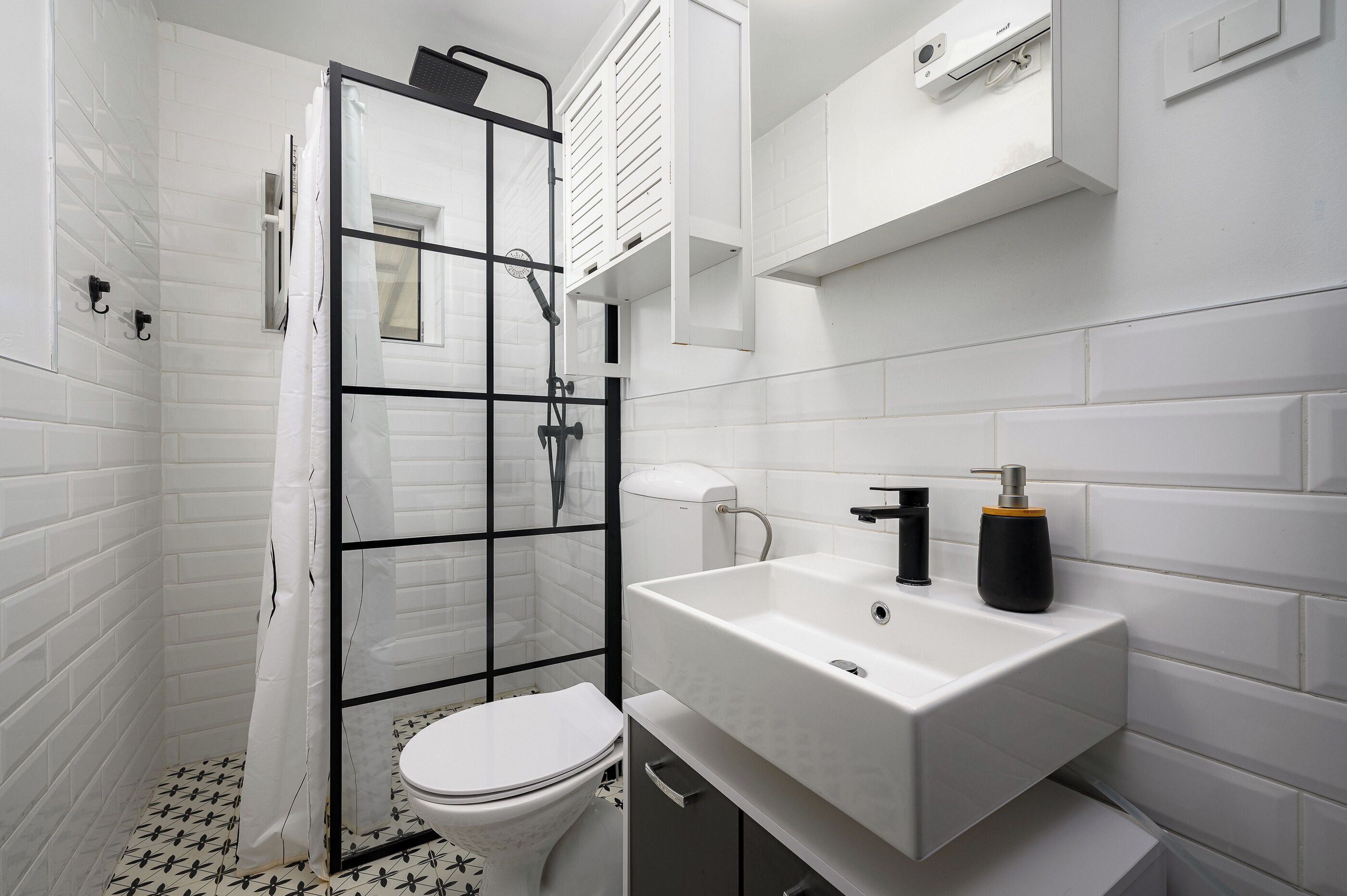 A modern bathroom with a glass shower enclosure, a white toilet, and a white sink with a black soap dispenser.