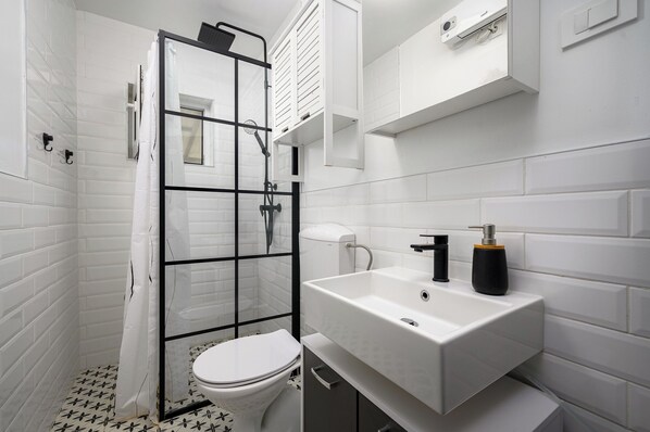 A modern bathroom with a glass shower enclosure, a white toilet, and a white sink with a black soap dispenser. - House Miha (Tar-Vabriga)