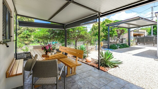 A covered patio with a wooden table and chairs, a bench, and a view of a garden and house. - House Miha (Tar-Vabriga)