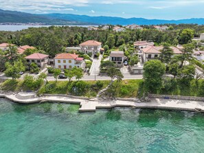 A coastal residential area with houses, clear turquoise waters, and a mountainous backdrop. - Apartments Nada (Dobrinj)