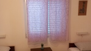 A room with two beds, a nightstand with a vase, and a window with patterned curtains. - House Garma (Blato)