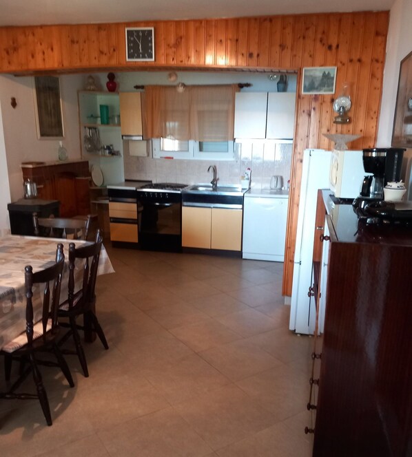 A kitchen with wooden cabinets, a stove, a sink, and a dining area with chairs. - House Garma (Blato)