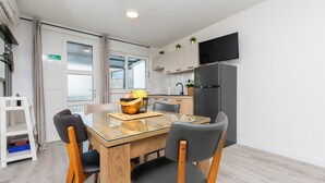 A modern kitchen with a built-in TV, a dining area with a glass table and wooden chairs, and a small refrigerator. - Apartment Golubinka (Dugi Rat)