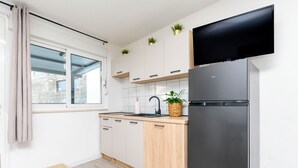 A modern kitchen with white cabinets, a stainless steel refrigerator, a wooden countertop, and a window with a view of a brick wall. - Apartment Golubinka (Dugi Rat)