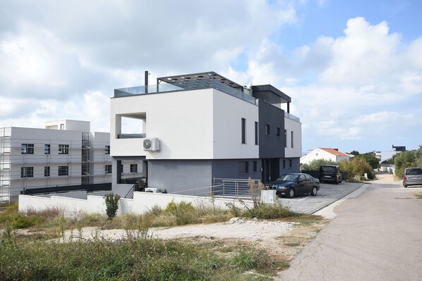 A modern two-story residential building with a flat roof, large windows, and a visible air conditioning unit. - Apartment Tin (Sveti Filip i Jakov)