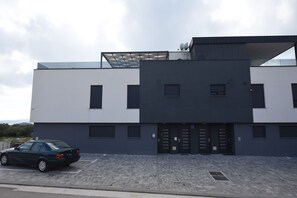 A modern building with a flat roof, multiple windows, and a car parked in front. - Apartment Tin (Sveti Filip i Jakov)
