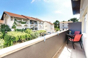 A balcony with a red chair and a small table, overlooking a courtyard with a building with a red roof and balconies. - Apartments Darinka (Vodice)