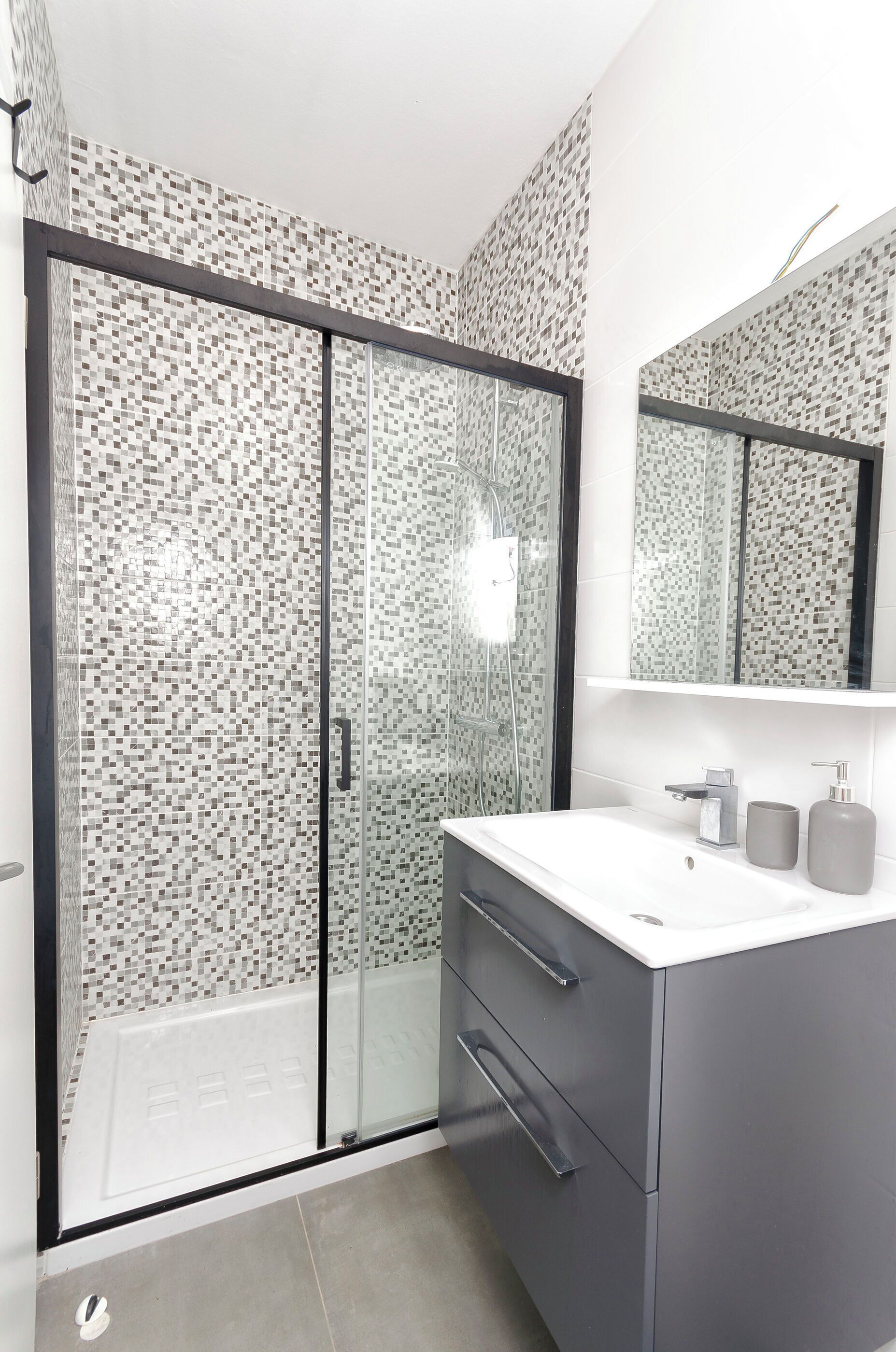 Un baño moderno con cabina de ducha de vidrio, un lavabo blanco y un espejo encima.
