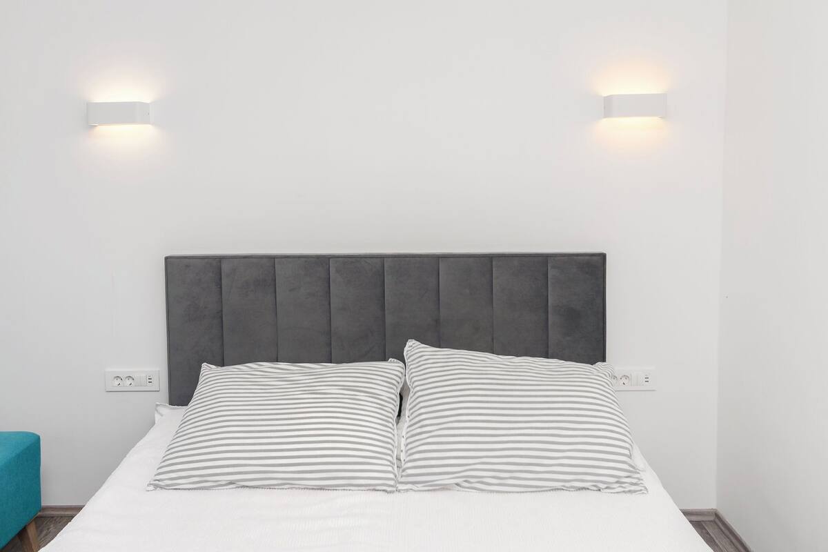 A bed with a grey upholstered headboard, two bedside lamps, and striped pillows.