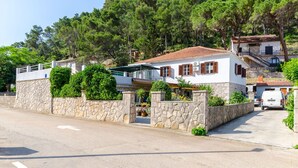 A two-story house with a stone facade, a tiled roof, and a driveway leading to a parked white van. - Apartment Kokic (Jelsa)