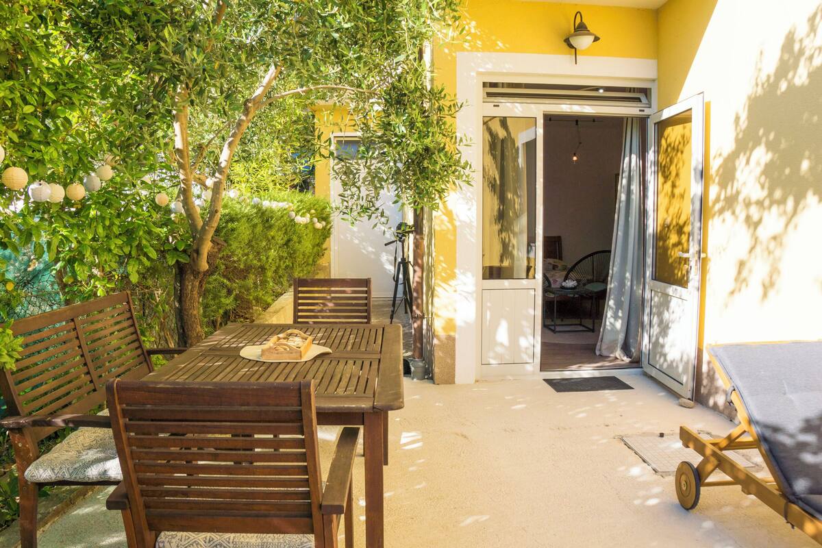 An outdoor patio with wooden furniture, a table, and a sun lounger.