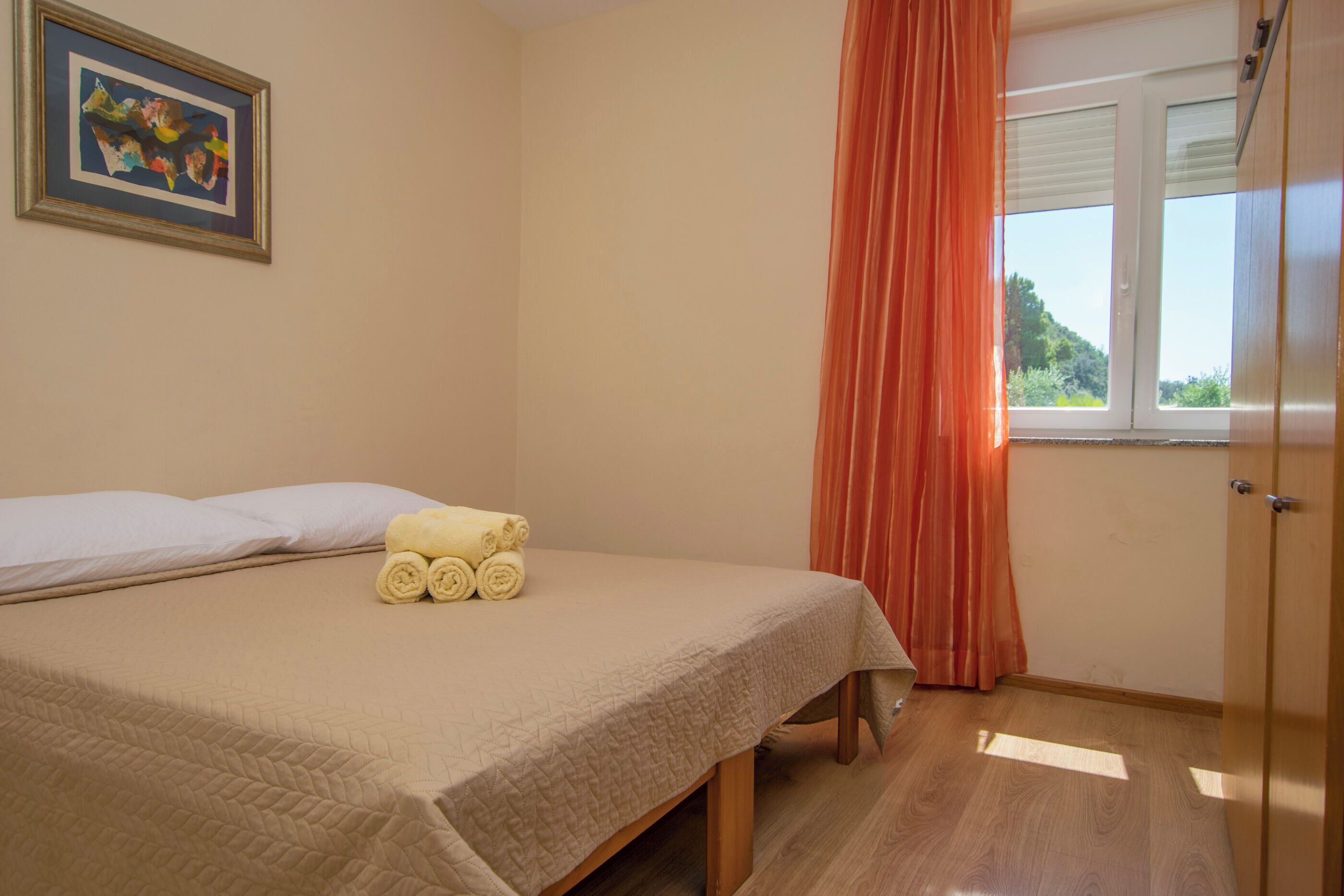 A bedroom with a bed, a window with curtains, and a painting on the wall.