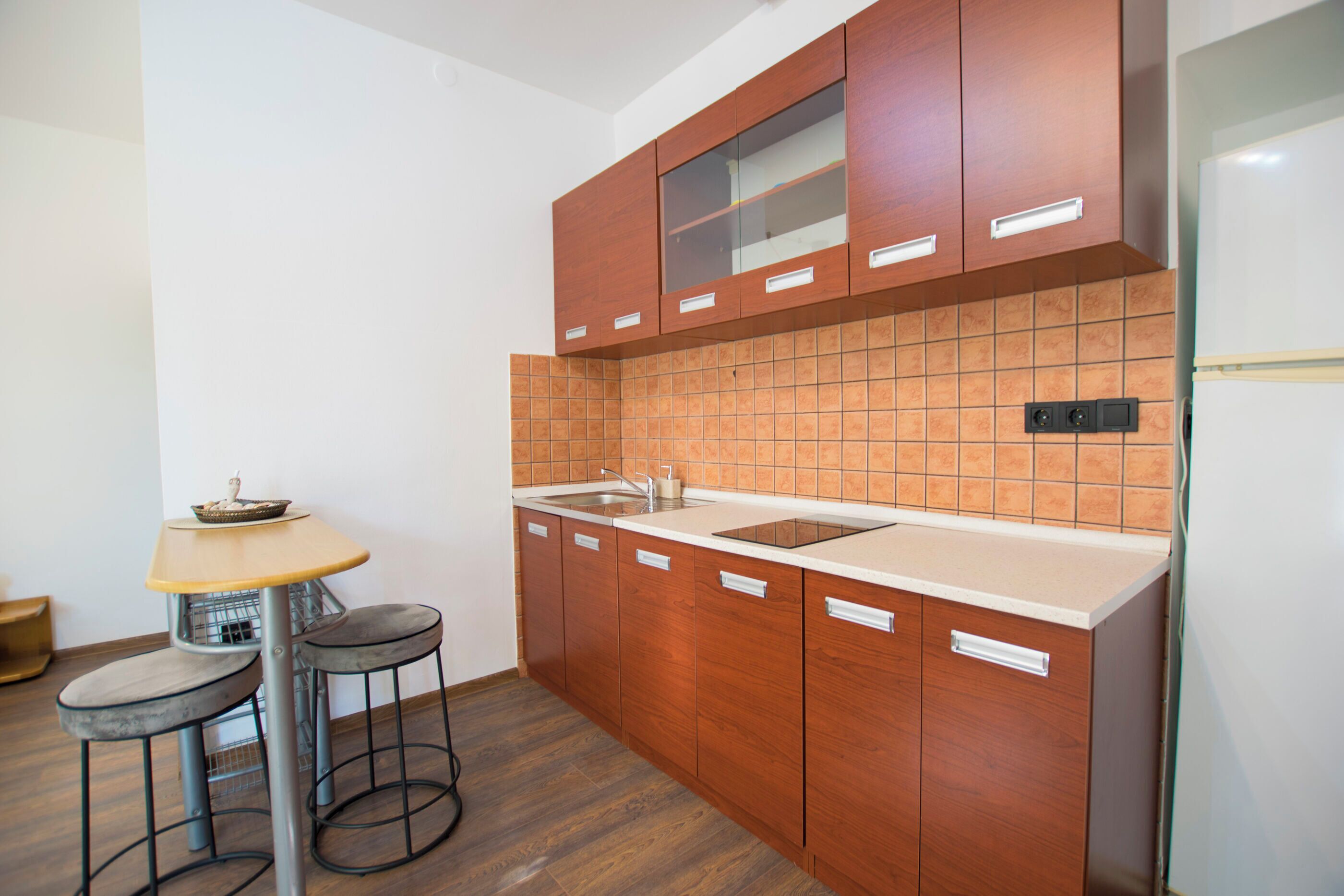 A compact kitchen with wooden cabinets, a sink, and a small dining table with stools.