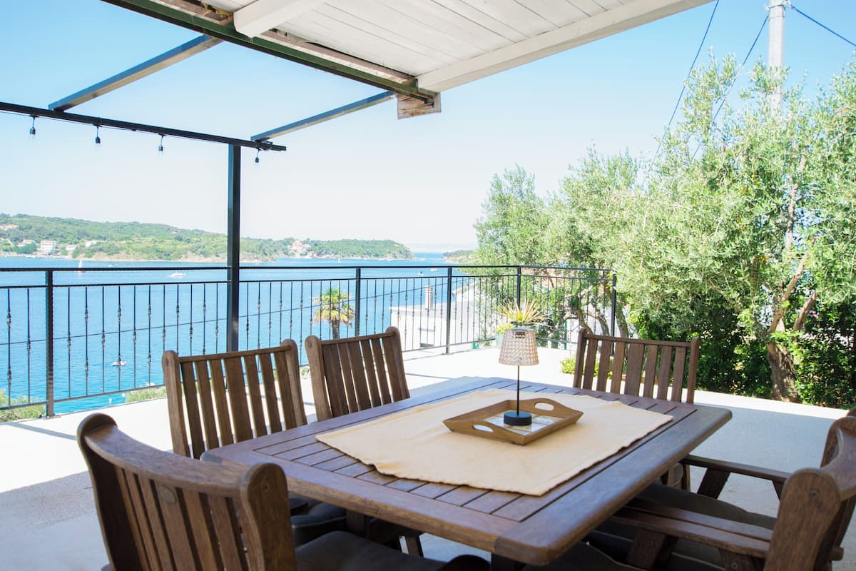 A wooden table and chairs on an outdoor patio with a view of the sea and hills.
