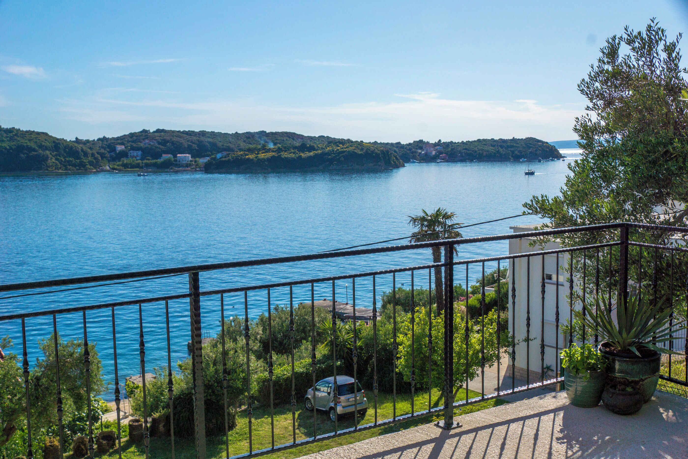 A balcony with a view of a lake, a parked car, and potted plants.