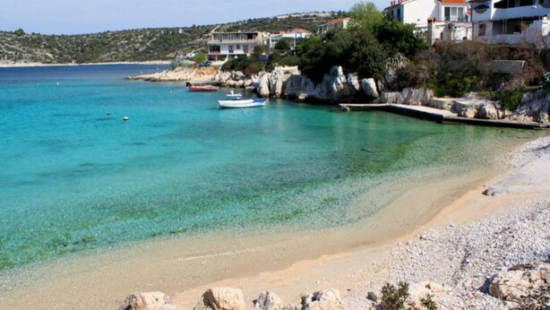 A coastal scene with clear turquoise water, a sandy beach, and rocky outcrops. - Apartments Marija (Rogoznica)
