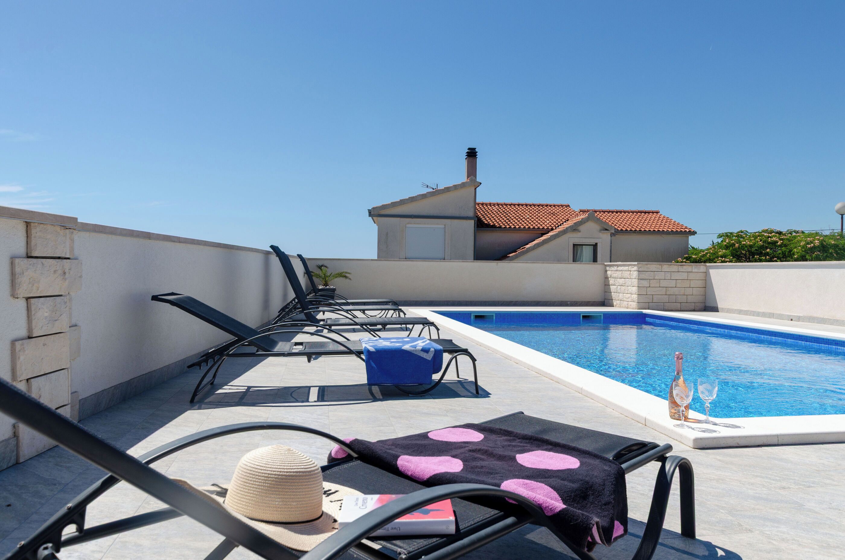 A rooftop pool area with lounge chairs, a pool, and a building with a tiled roof.