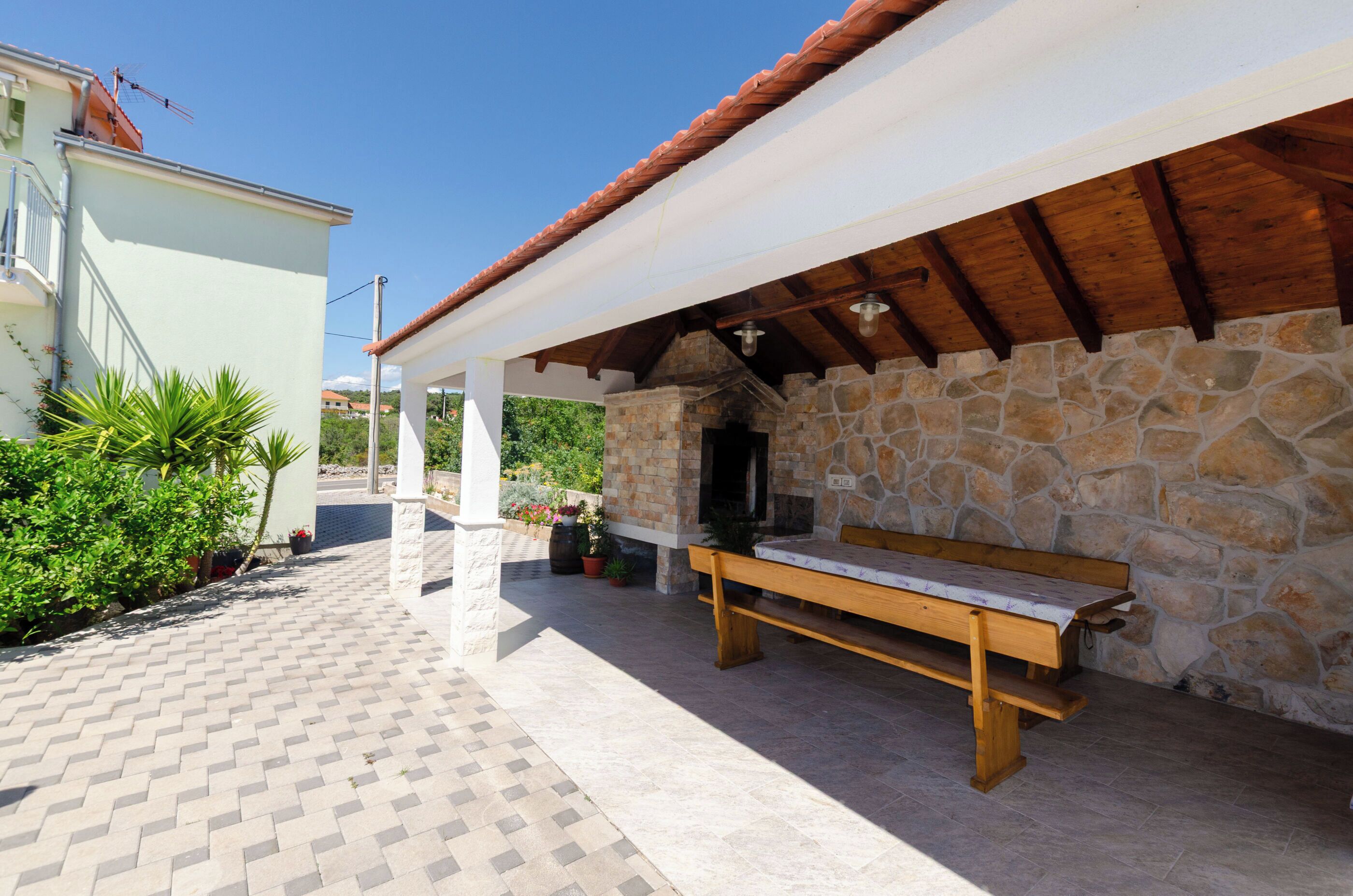 Un'area salotto esterna coperta con un muro in pietra, una panchina di legno e un patio piastrellato.