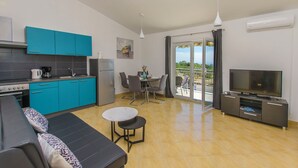 A modern kitchen with blue cabinets, a dining area with a table and chairs, a sofa, and a TV. - Apartments Marija (Rogoznica)