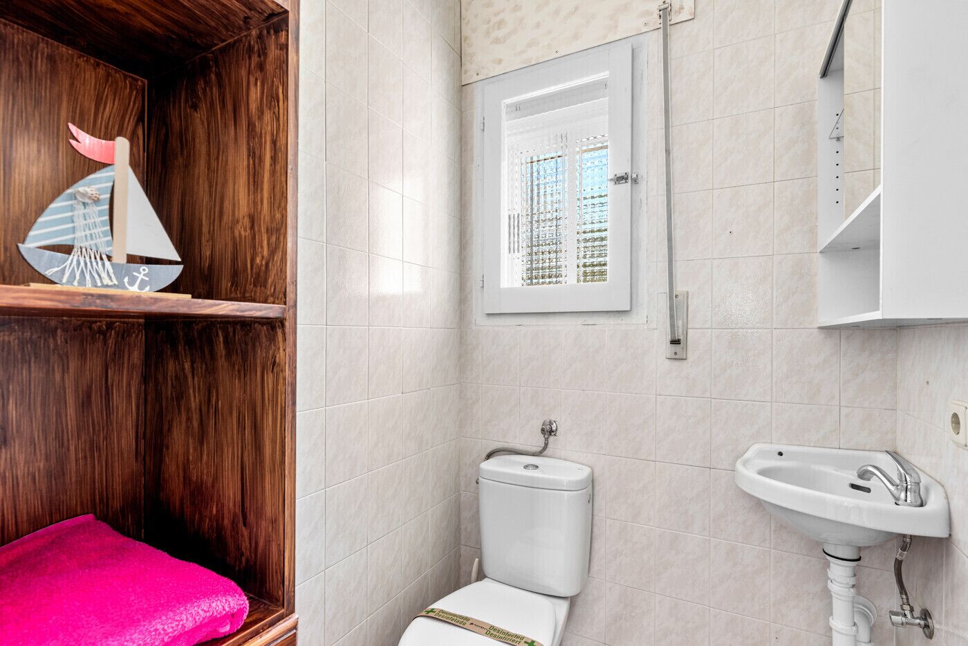 A bathroom with a wooden vanity, a toilet, a sink, and a window with a view of buildings.