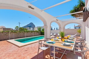 A rooftop terrace with a pool, dining table set for two, and a view of a mountain and cityscape. - Villa Venus - Plusholidays (Calpe)