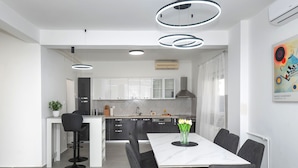 Uma cozinha moderna com armários brancos, uma ilha central e um espaço de jantar com mesa e cadeiras brancas.