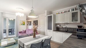 A modern kitchen with white cabinets, a dining area with a table and chairs, and a large window with curtains. - House Cetiri Hrasta (Pican)