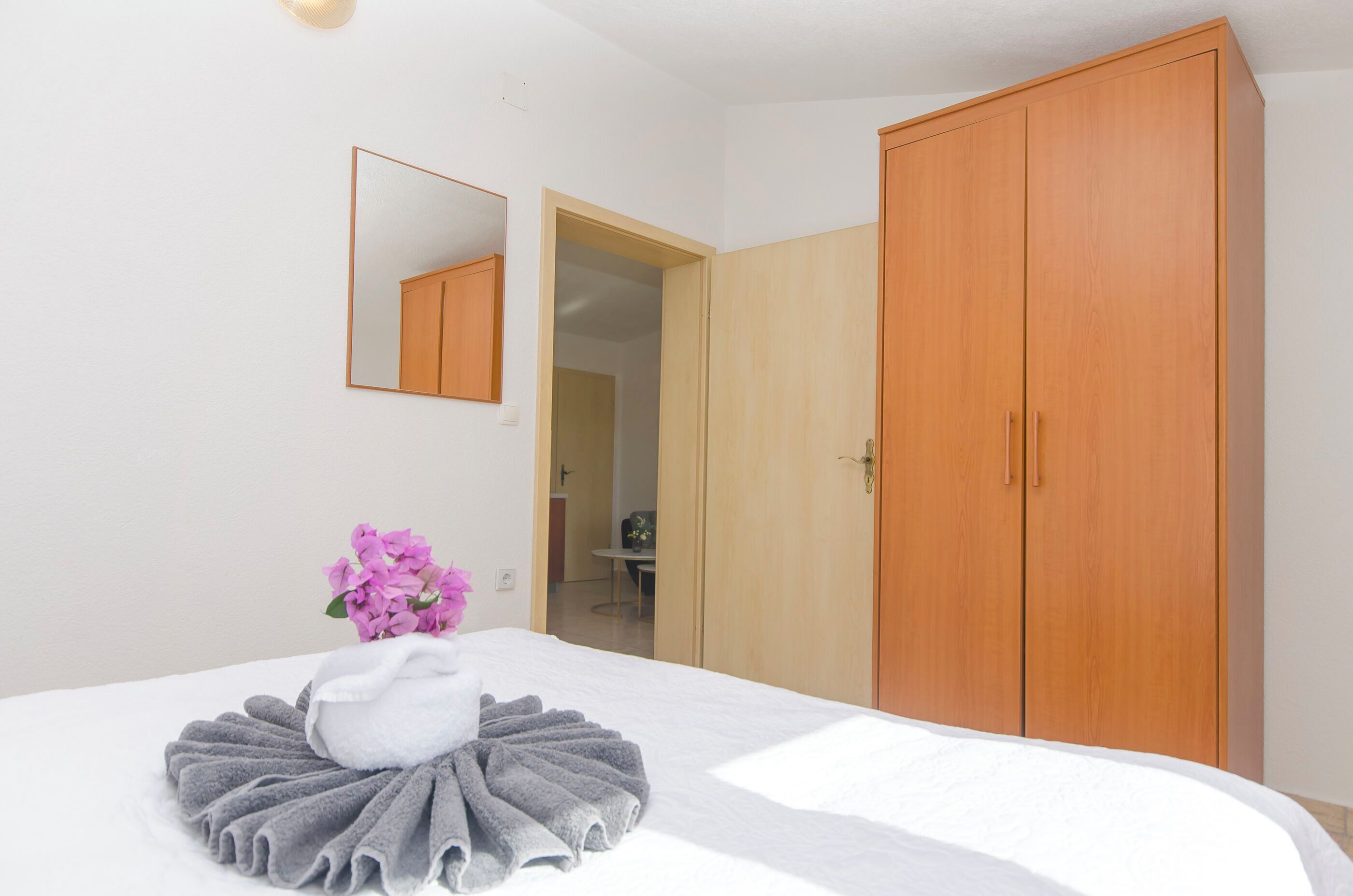 Un dormitorio con cama, armario de madera, espejo y baño visible a través de una puerta abierta.