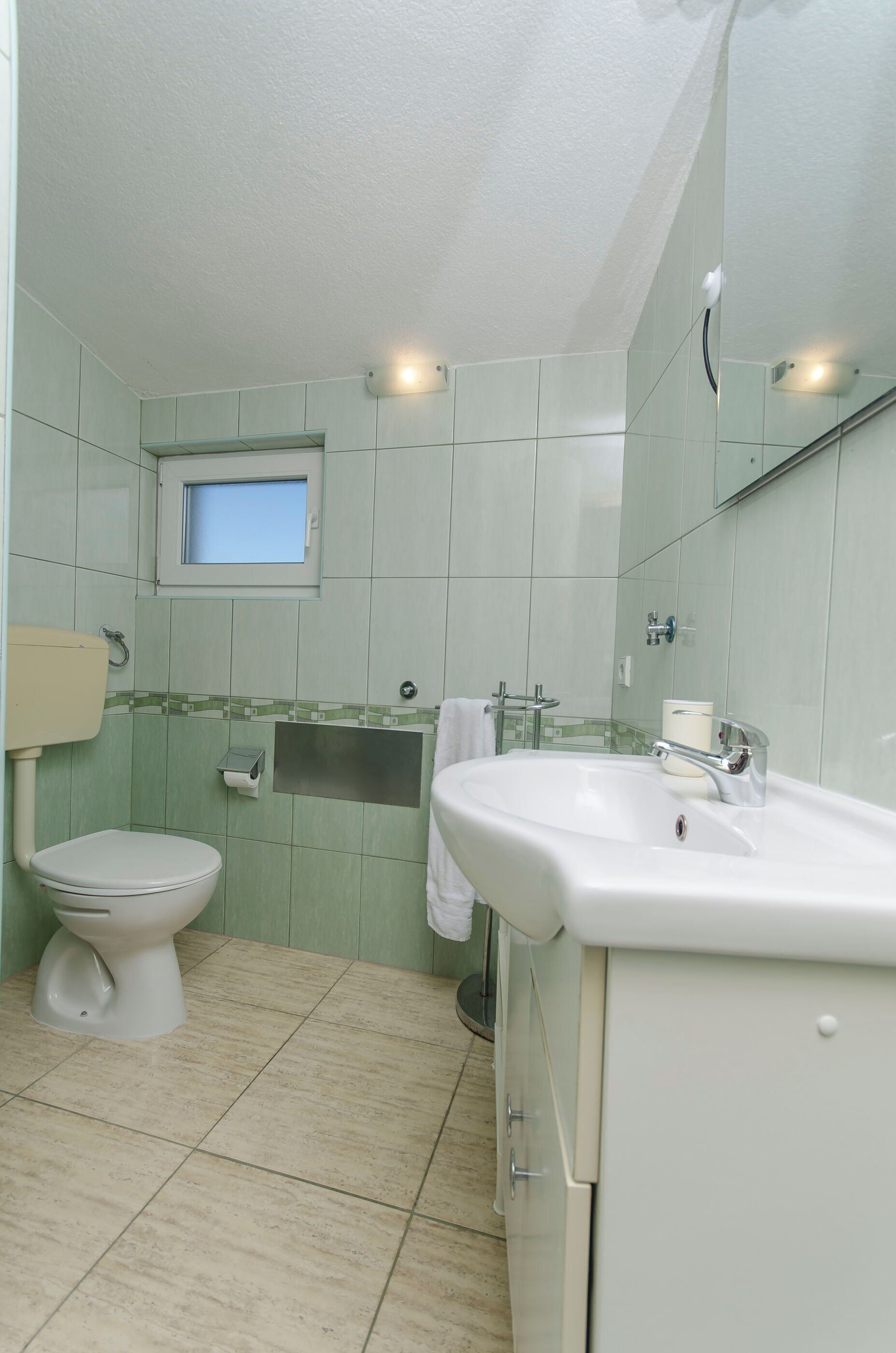 Een badkamer met toilet, wastafel en een klein raam.