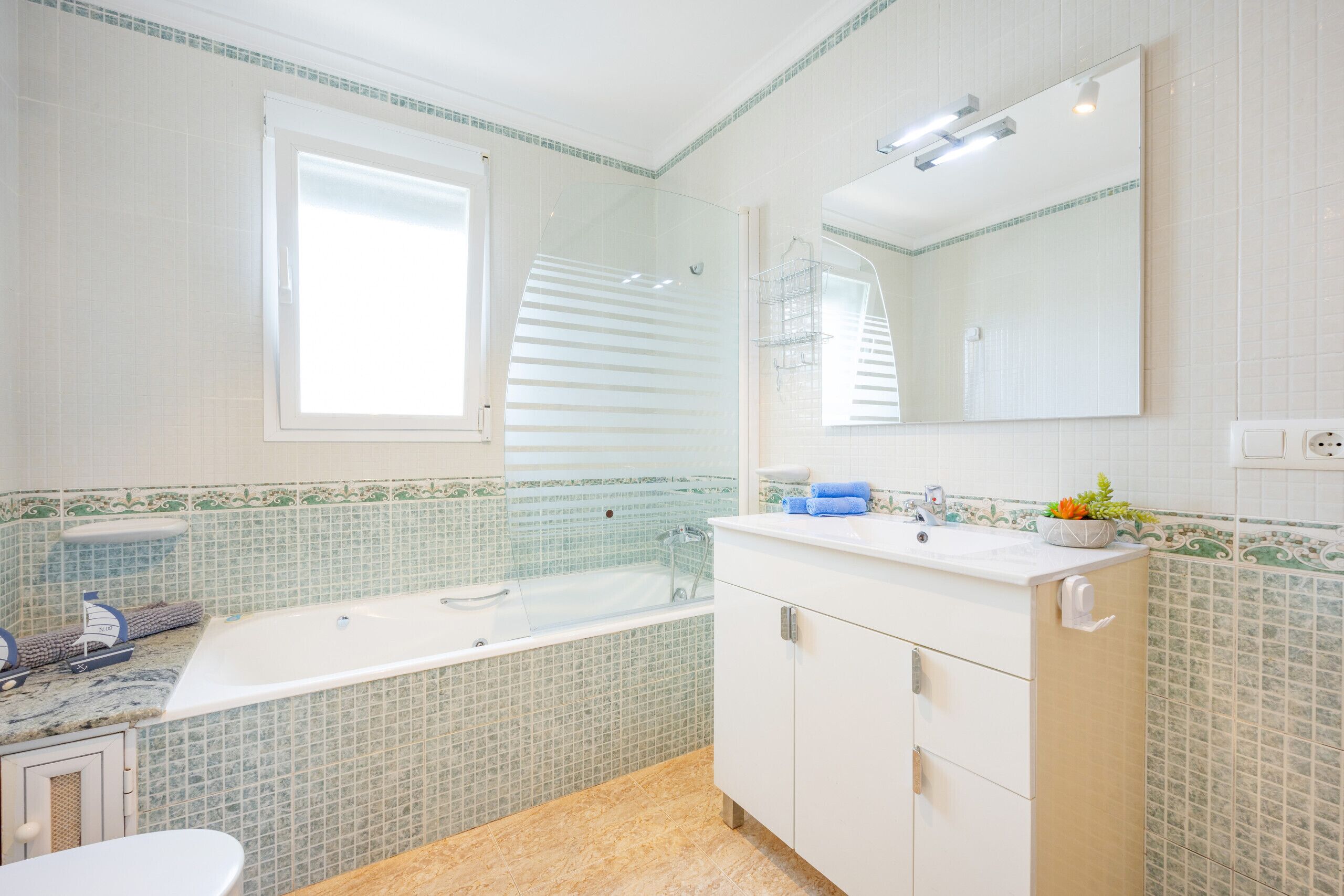 A bathroom with a bathtub, a sink, a mirror, and a window.