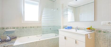 A bathroom with a bathtub, a sink, a mirror, and a window.