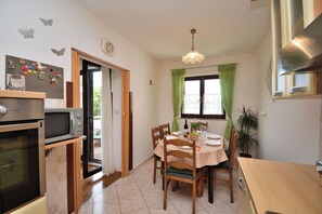 Een keuken met een eettafel, stoelen, een magnetron, oven en een hanglamp.