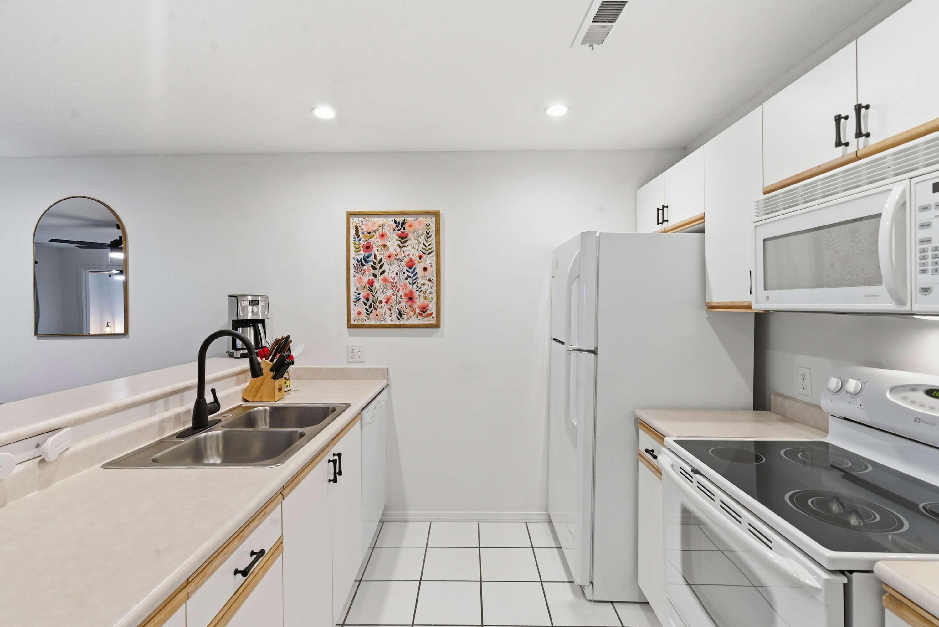 A modern kitchen with white cabinets, a stainless steel sink, a microwave, a stove, and a refrigerator.