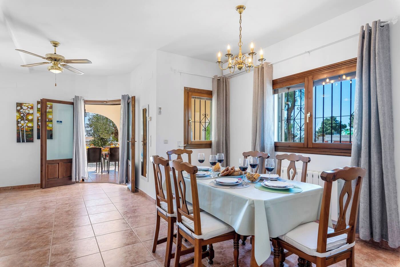 A dining area with a table set for four, chairs, a chandelier, and a view through the window.