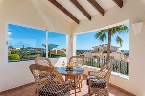 A balcony with wicker furniture, a round table, and a view of a coastal landscape. - Villa Azur - Plusholidays (Calpe)