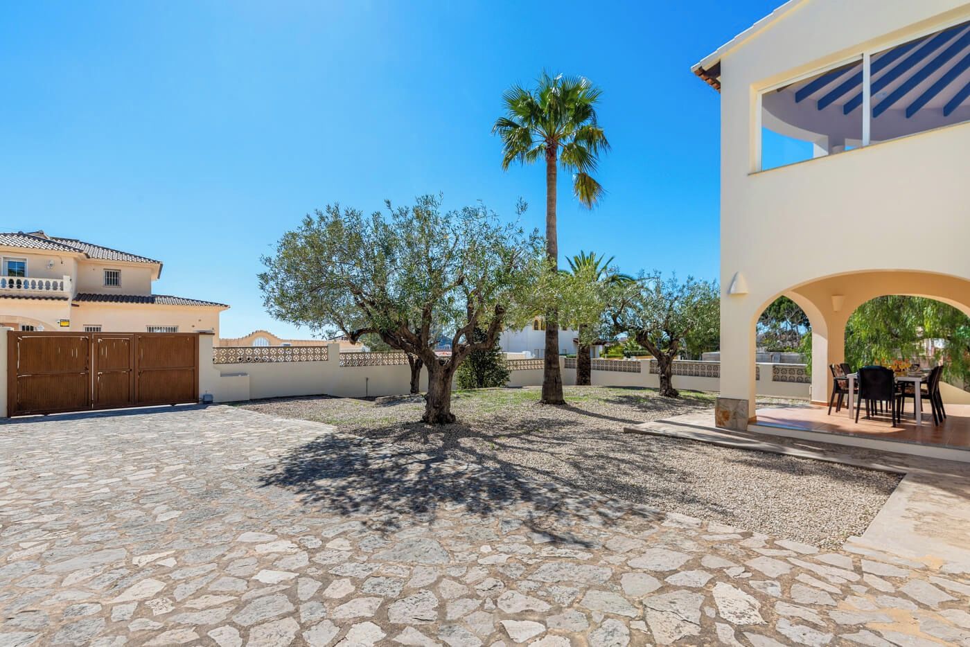 A courtyard with stone flooring, palm trees, and a building with an archway.