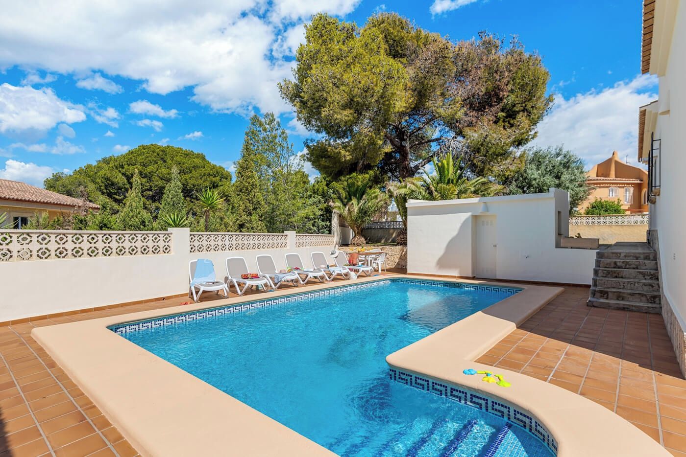 Una piscina con sillones de descanso y una pared blanca con un diseño decorativo.