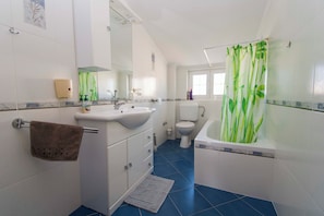 A bathroom with a white sink, mirror, and toilet, a blue tiled floor, and a green shower curtain. - Apartments Milenko (Vodice)