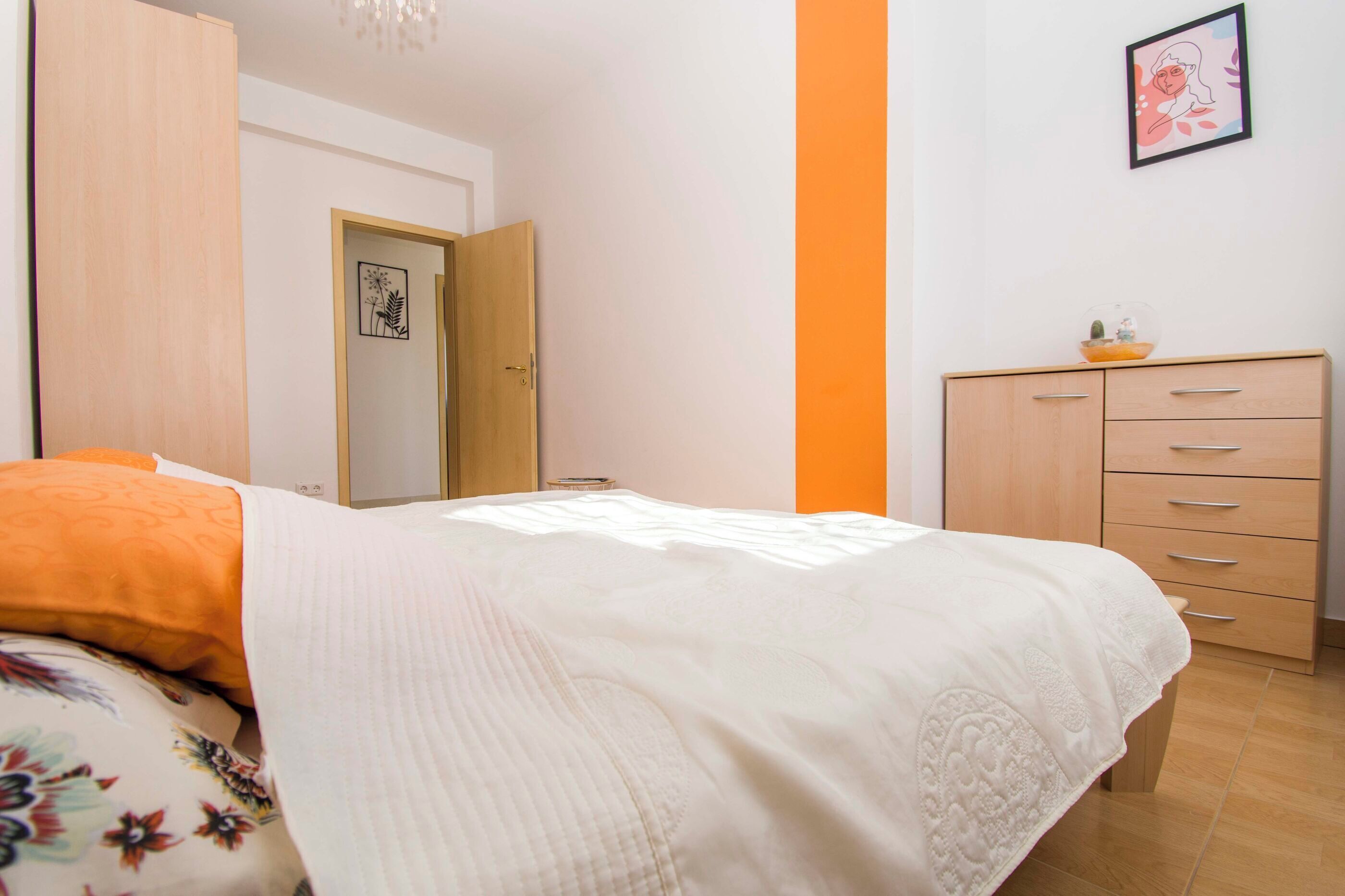 A bedroom with a bed, a dresser, a door, and a wall with a picture.