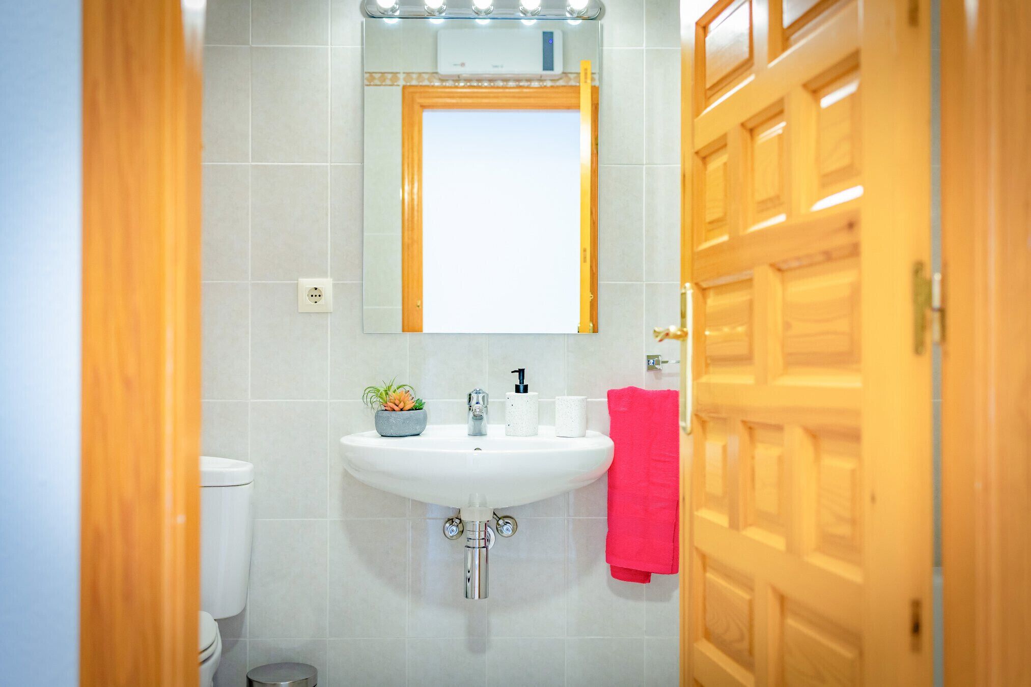 Un baño con un lavamanos blanco, un espejo y una toalla roja colgada en la pared.