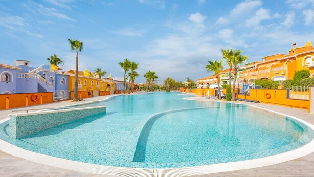Una piscina amplia y cristalina rodeada de edificios coloridos con balcones y palmeras.