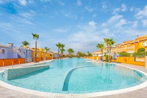 Una piscina amplia y cristalina rodeada de edificios coloridos con balcones y palmeras.